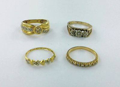 quatre bagues en or serties de diamants, posées sur une surface blanche