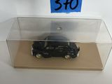une petite voiture noire dans une boîte transparente sur laquelle est collé un autocollant bleu