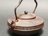 a small copper teapot with a handle on a table