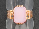bague en verre rose rehaussée de touches dorées, posée sur un socle en acrylique transparent