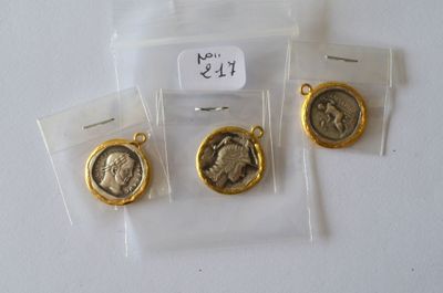 trois médailles en or et en argent dans des sachets en plastique, posées sur une surface blanche