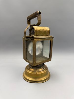 une vieille lanterne en laiton posée sur une surface blanche, avec un fond gris