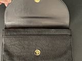 a hand holding a black purse with a gold button