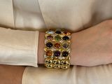 a woman wearing a gold bracelet with multi colored stones on it