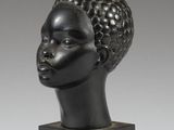 une sculpture noire représentant la tête d'une femme, posée sur un socle noir