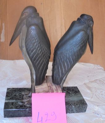 two statues of birds sitting on a table with a pink note