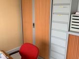 a red chair in the corner of a room next to a filing cabinet