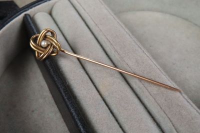 une broche en or sertie d'une perle, posée dans un écrin