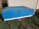 a blue tarp covering a bed in the grass