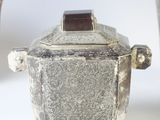 a silver container with a lid sitting next to a silver cup