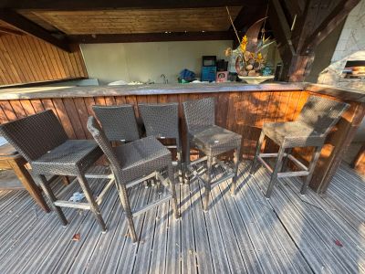 quatre chaises en osier posées sur une terrasse en bois près d'un bar