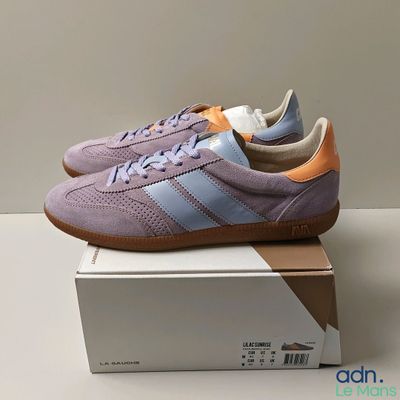 des baskets Adidas violettes posées sur une boîte, sur une surface blanche