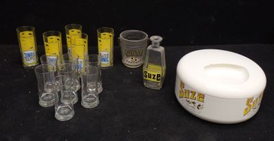 Des bouteilles et des verres sont alignés sur une table, à côté d'un récipient blanc.