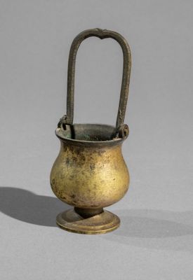 an old brass vase with a handle on a gray surface