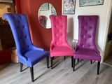 deux chaises violettes et une bleue dans une pièce où un miroir est accroché au mur