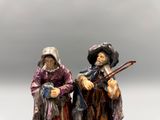 two figurines of two men with hats and canes on a white surface
