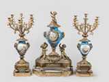 trois types de vases différents et une horloge posés sur une table