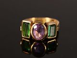 un gros plan d'une bague en or sertie d'une pierre violette et verte