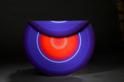 purple and red vase sitting on a black surface with a book in the background