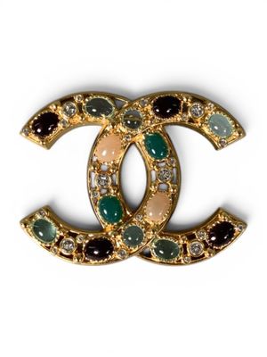 a close up of a chanel brooch with green and white stones