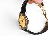 a person holding a wrist watch with a gold face