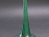 a green vase sitting on top of a table next to a gray wall