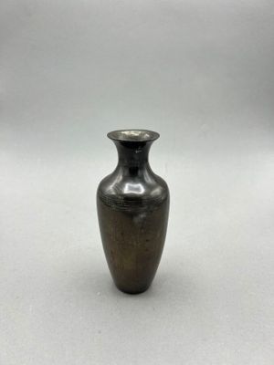 a small metal vase sitting on a white surface