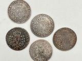 cinq pièces d'argent ornées d'une couronne, posées sur une surface blanche