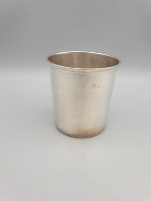 une coupe en argent munie d'une anse, posée sur une surface blanche