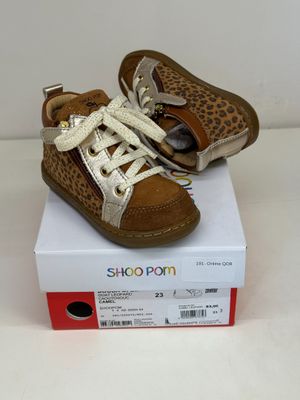 des chaussures de bébé marron et blanches ornées d'un imprimé léopard, posées sur une boîte