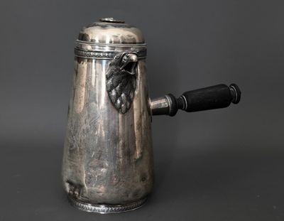 une cafetière ancienne en argent, avec une poignée noire sur fond gris