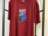 un t-shirt rouge représentant un casque, suspendu à un cintre devant un mur blanc