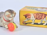 un petit chat en peluche qui joue avec une balle devant une boîte