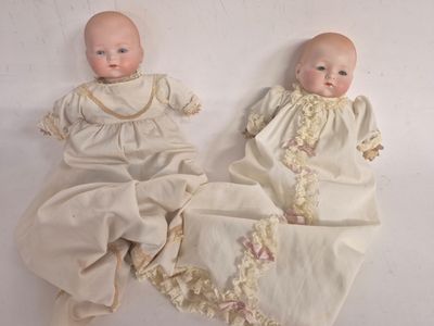 two baby dolls laying next to each other on a white surface