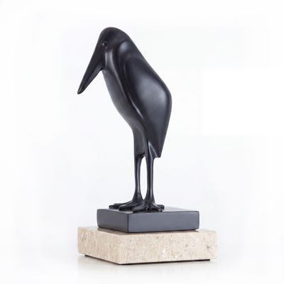 statue d'un oiseau noir posée sur un socle en marbre, sur fond blanc
