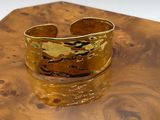 gold plated cuff bracelet on a wooden box on a white background