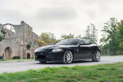 une voiture de sport noire qui roule sur la route devant un vieux bâtiment