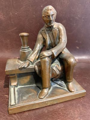 bronze statue of a man sitting on a bench with a vase