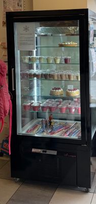 une femme debout devant une vitrine remplie de gâteaux