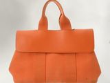 an orange leather handbag with a long strap on a white background