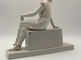 statue of a woman sitting on a block with her hands on her knees
