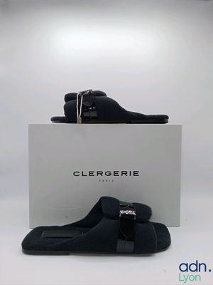 Les chaussons noirs se trouvent à côté d'une boîte blanche, posée sur une surface blanche.