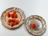 two silver plates with oranges in them on a white table