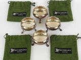 six bols plaqués argent, accompagnés de pochettes en velours vert, posés sur un fond blanc