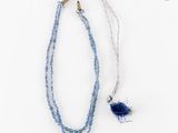 collier composé de perles de verre bleues et d'une breloque en forme de plume bleue sur fond blanc