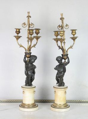 paire de bougeoirs anciens en bronze ornés de chérubins, posés sur des socles en marbre