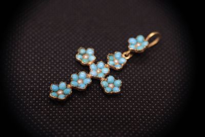 a gold cross pendant with turquoise stones on a black background