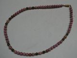Collier de perles roses et noires rehaussé de touches dorées sur un fond blanc