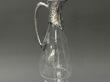 an antique glass pitcher with a silver handle on a gray background