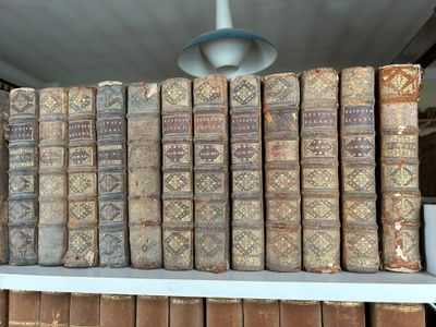 de nombreux livres anciens empilés sur une étagère dans une pièce